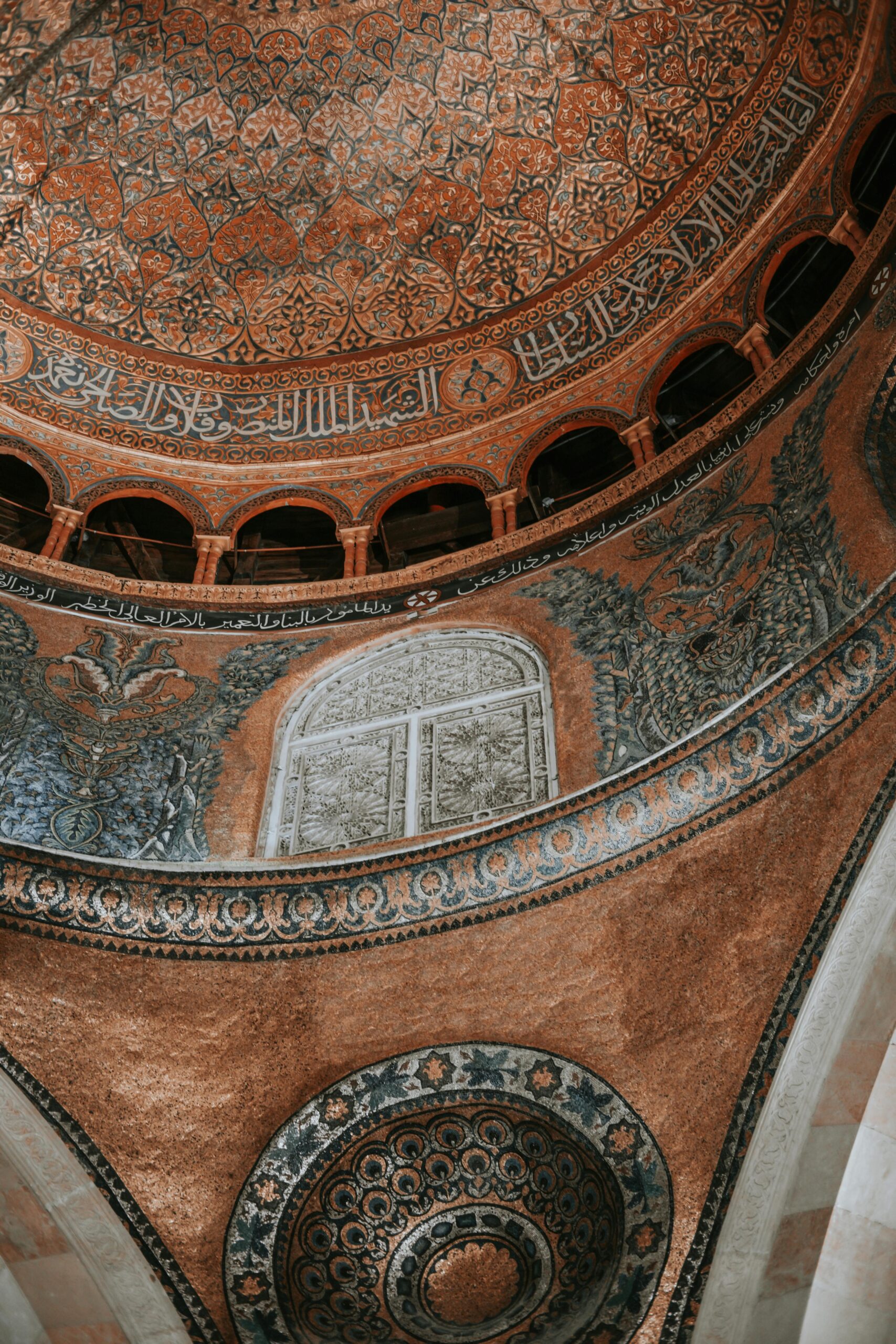 Intricate interior view of a dome with detailed Islamic patterns and Arabic calligraphy.